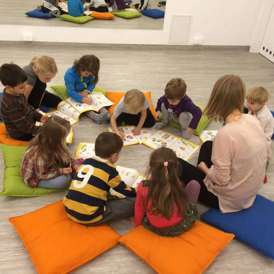 Dzieci z lektorką czytają podręczniki na kolorowych poduszkach